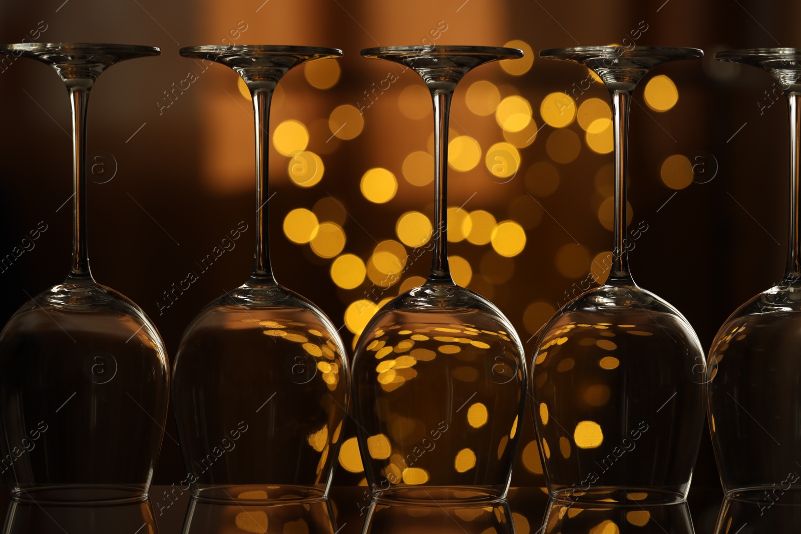 Photo of Many clean glasses on glass mirror surface against blurred lights, closeup. Bokeh effect