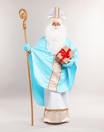 Photo of Saint Nicholas with Christmas gift and crozier on gray background