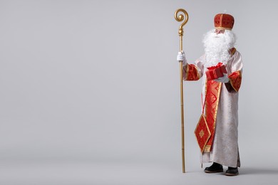 Photo of Saint Nicholas with gift on light grey background. Space for text