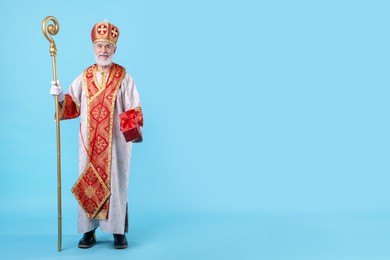 Photo of Saint Nicholas with gift on light blue background. Space for text