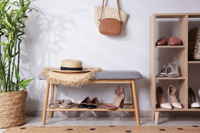 Photo of Stands with different stylish shoes, straw hats, bags and houseplant indoors