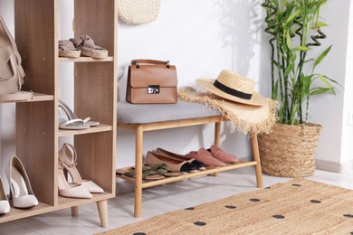 Photo of Stands with different stylish shoes, straw hats, bag and houseplant indoors