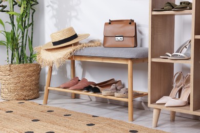 Photo of Stands with different stylish shoes, straw hats, bag and houseplant indoors