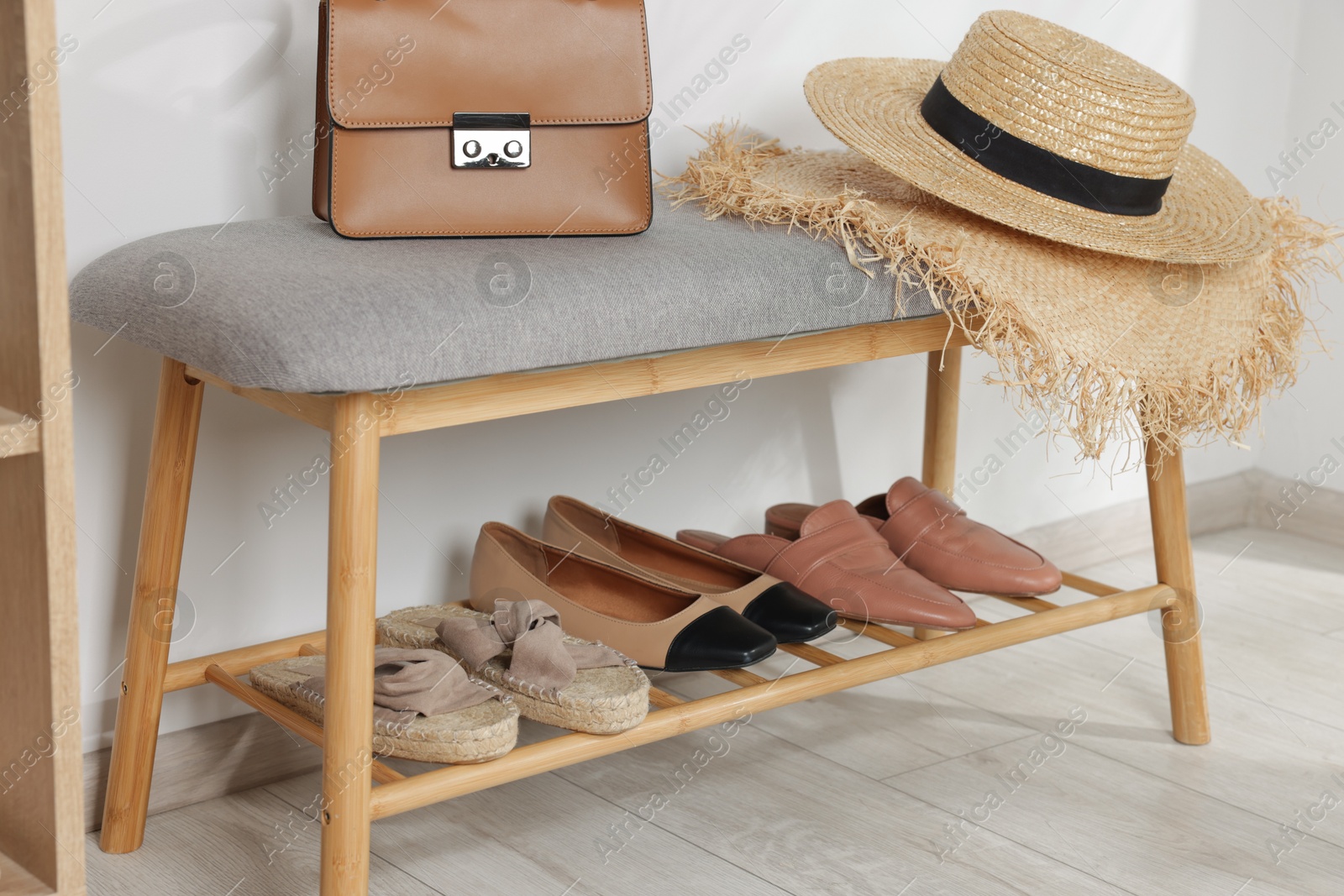 Stand with different stylish shoes, straw hats and bag indoors Photo of Stand with different stylish shoes, straw hats and bag indoors