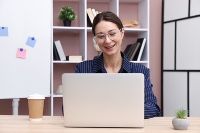 Photo of Smiling online speaker streaming webinar with laptop at table indoors