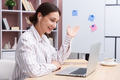 Photo of Smiling online speaker streaming webinar with laptop at table indoors