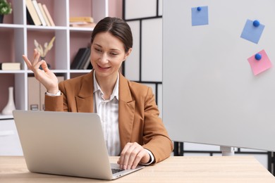 Photo of Smiling online speaker streaming webinar with laptop at table indoors