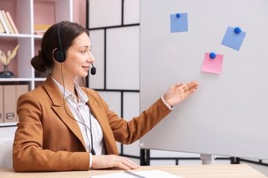 Photo of Smiling online speaker in headset performing webinar near flip chart indoors