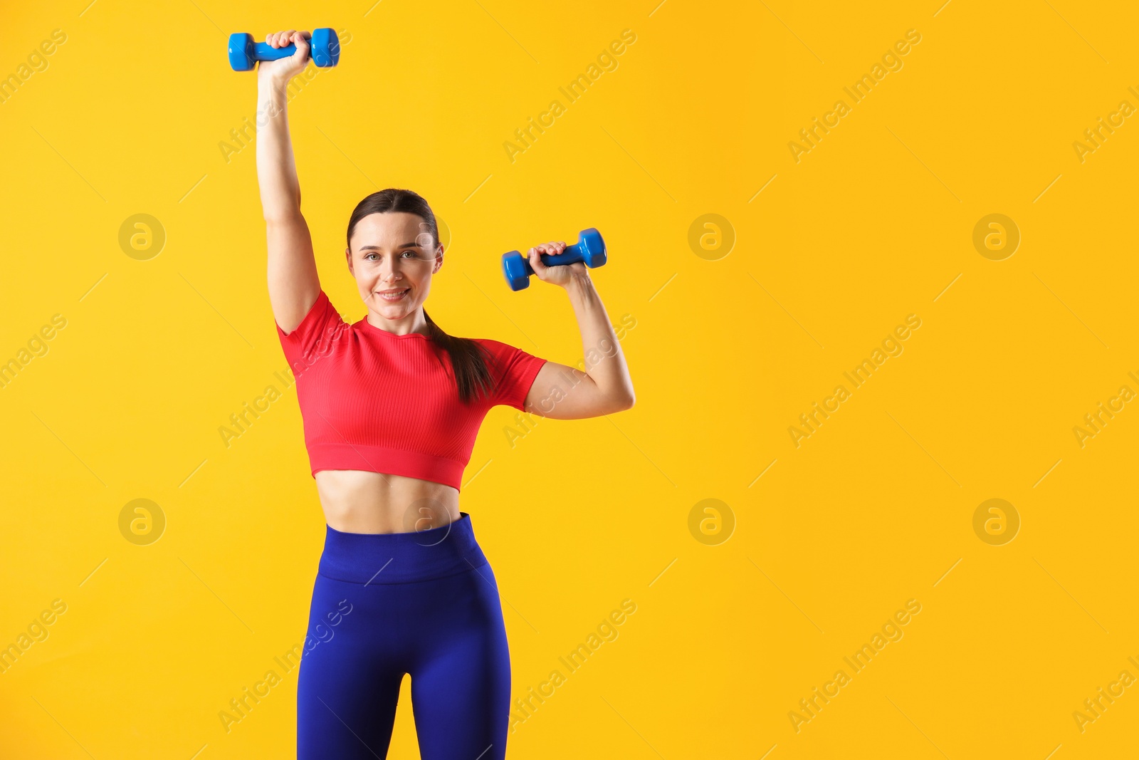 Photo of Woman in sportswear exercising with dumbbells on orange background, space for text