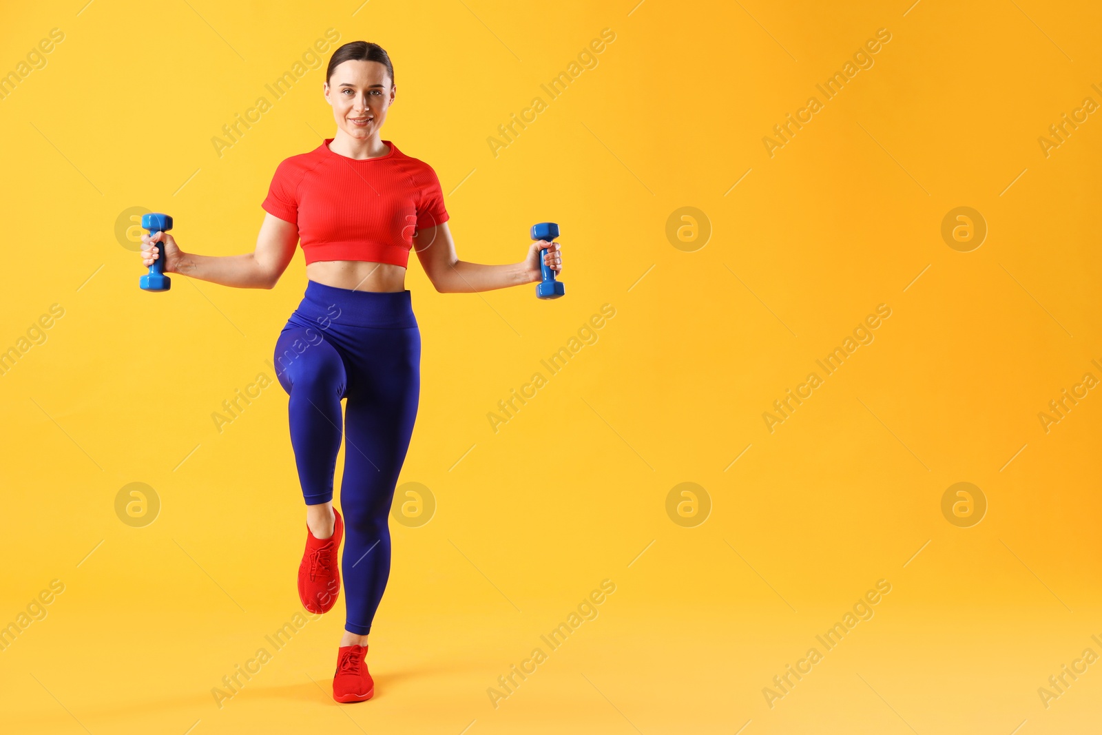 Photo of Woman in sportswear exercising with dumbbells on orange background, space for text