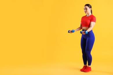 Photo of Woman in sportswear exercising with dumbbells on orange background, space for text