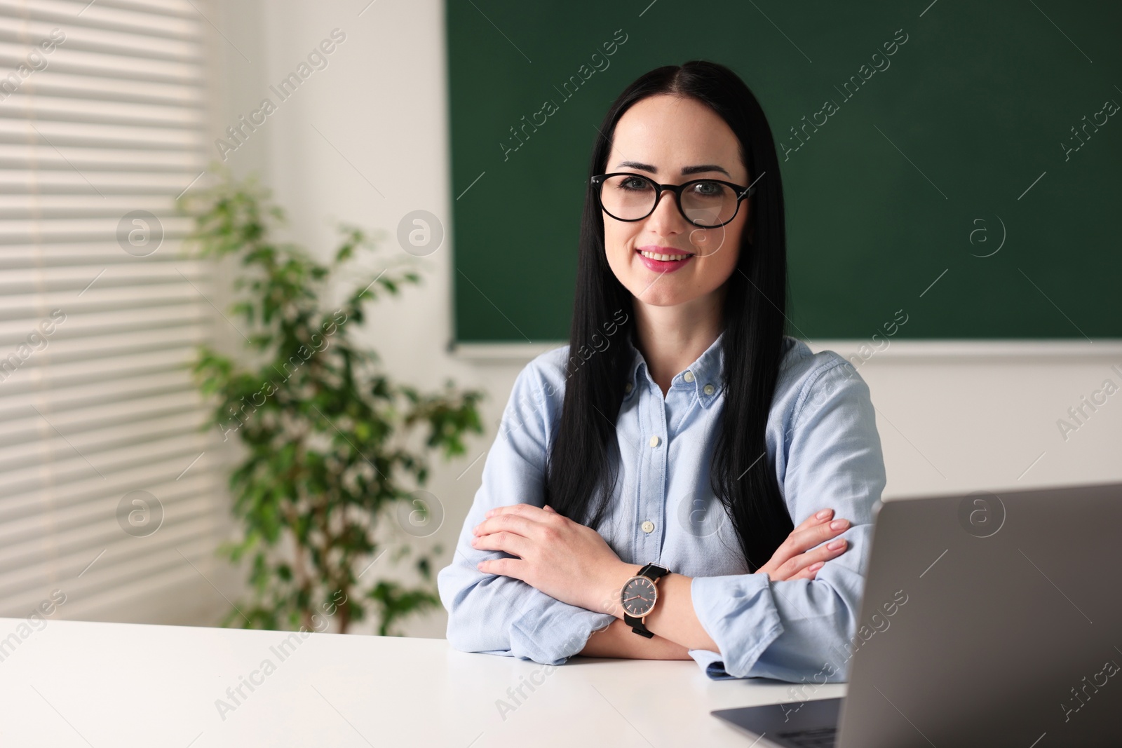 Photo of English teacher with laptop at desk in classroom. Space for text