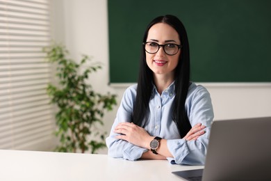 Photo of English teacher with laptop at desk in classroom. Space for text