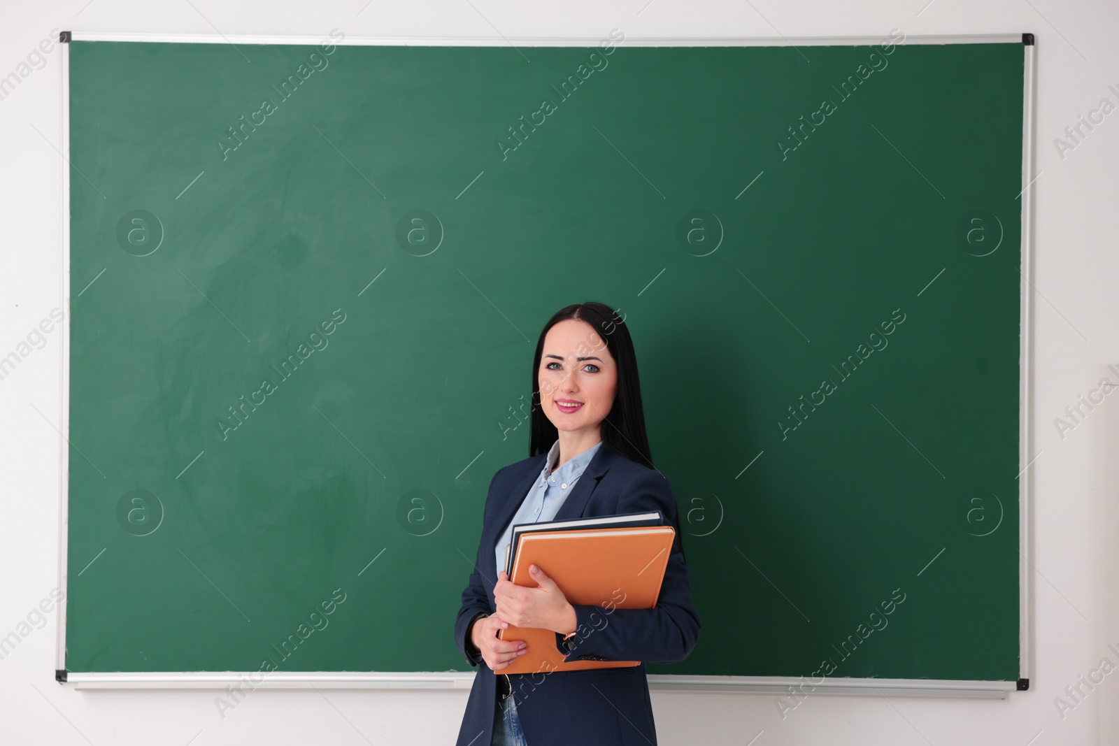 Photo of English teacher with books near chalkboard in classroom