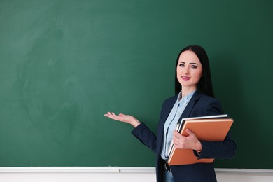 Photo of English teacher with books near chalkboard in classroom. Space for text