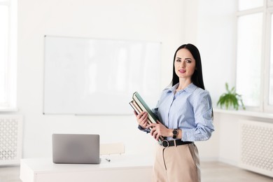 Photo of English teacher with books at desk in classroom. Space for text