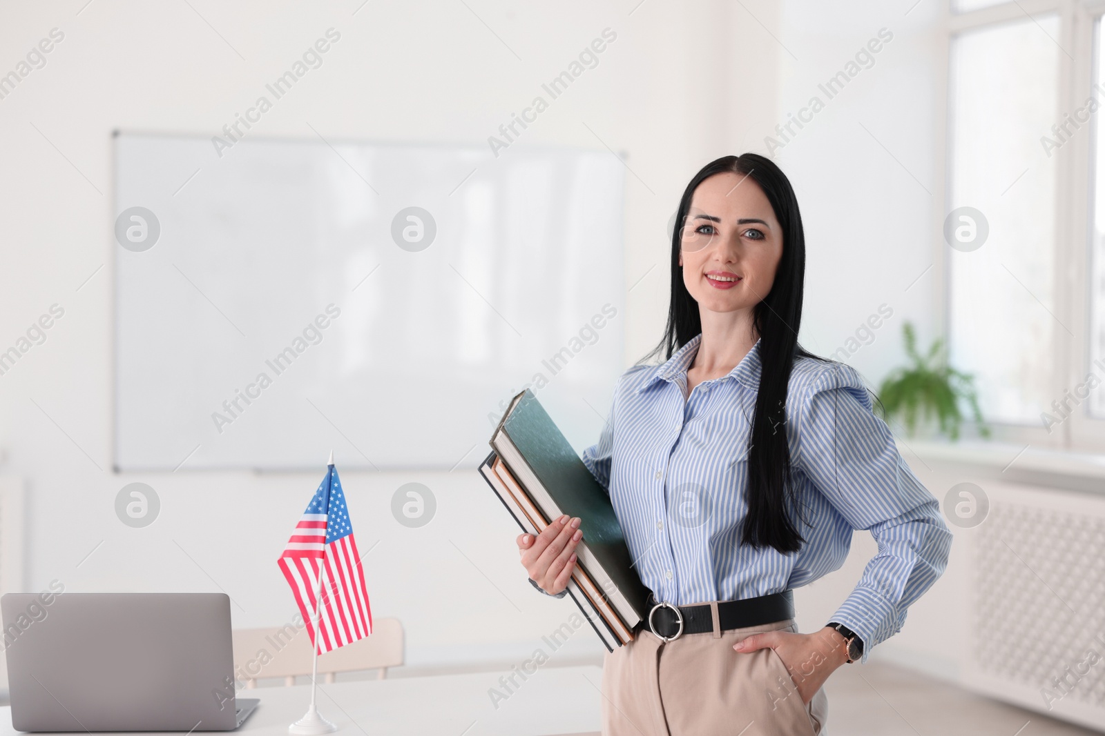 Photo of English teacher with books at desk in classroom. Space for text