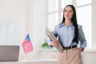 Photo of English teacher with books at desk in classroom. Space for text