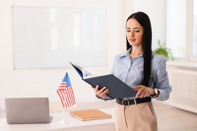 Photo of English teacher with book at desk in classroom. Space for text