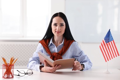 Photo of English teacher with book at desk in classroom