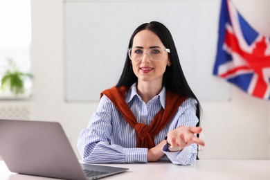 Photo of English teacher working on laptop at desk in classroom