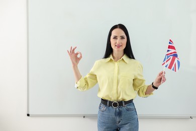 Photo of English teacher showing ok gesture near whiteboard in classroom