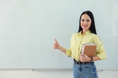 Photo of English teacher showing thumbs up near whiteboard in classroom. Space for text