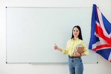 Photo of English teacher showing thumbs up near whiteboard in classroom. Space for text