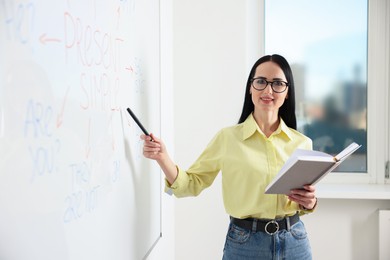 Photo of English teacher explaining Present Simple tense at whiteboard in classroom