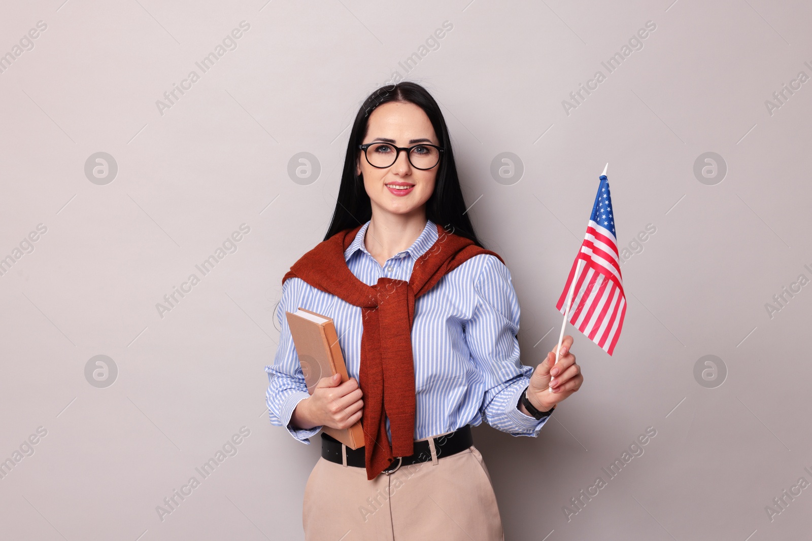 Photo of English teacher with book and American flag on light grey background