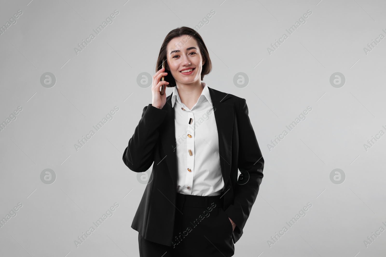 Photo of Smiling secretary talking on smartphone against grey background