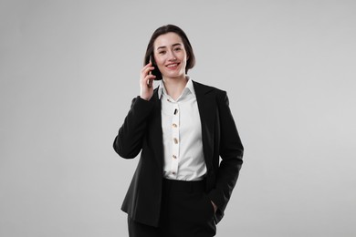 Photo of Smiling secretary talking on smartphone against grey background