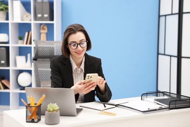 Photo of Secretary with glasses using smartphone at table in office