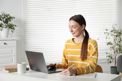 Photo of Woman taking notes during online lesson at table indoors. Self-study