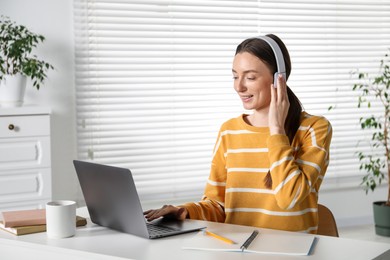 Photo of Smiling woman learning online using laptop at table indoors. Self-study