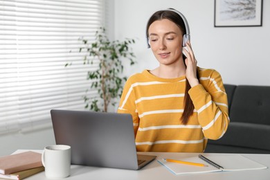 Photo of Smiling woman learning online using laptop at table indoors