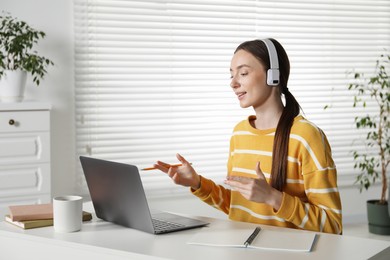 Photo of Smiling woman having online lesson with teacher by laptop at table indoors