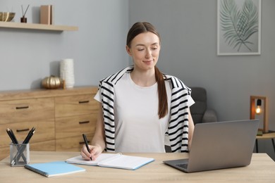 Photo of Woman taking notes during online lesson at table indoors. Self-study