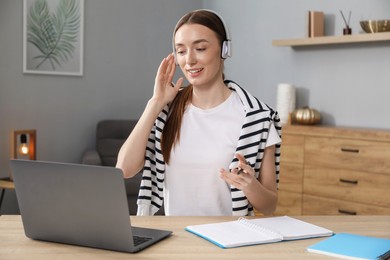 Photo of Smiling woman having online lesson with teacher by laptop at table indoors