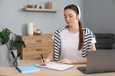 Photo of Woman taking notes during online lesson at table indoors. Self-study