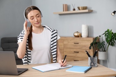 Photo of Woman taking notes during online lesson at table indoors. Self-study