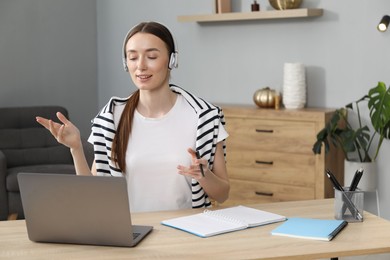 Photo of Smiling woman having online lesson with teacher by laptop at table indoors