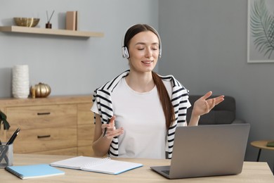 Photo of Smiling woman having online lesson with teacher by laptop at table indoors