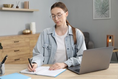 Photo of Woman taking notes during online lesson at table indoors. Self-study