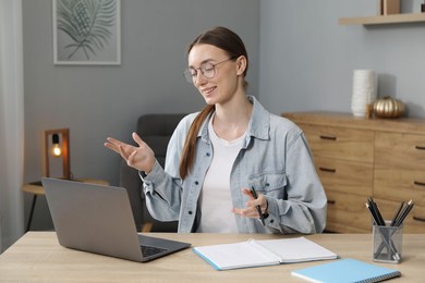 Photo of Smiling woman having online lesson with teacher by laptop at table indoors