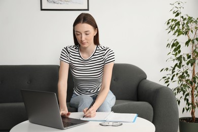 Photo of Woman taking notes during online lesson at table indoors. Self-study