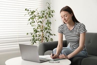 Photo of Woman taking notes during online lesson at table indoors. Self-study