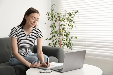 Photo of Woman taking notes during online lesson at table indoors. Self-study