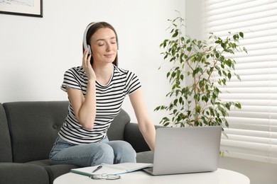 Photo of Woman learning online using laptop at table on sofa indoors. Self-study