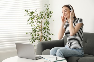 Photo of Woman learning online using laptop at table on sofa indoors, space for text. Self-study